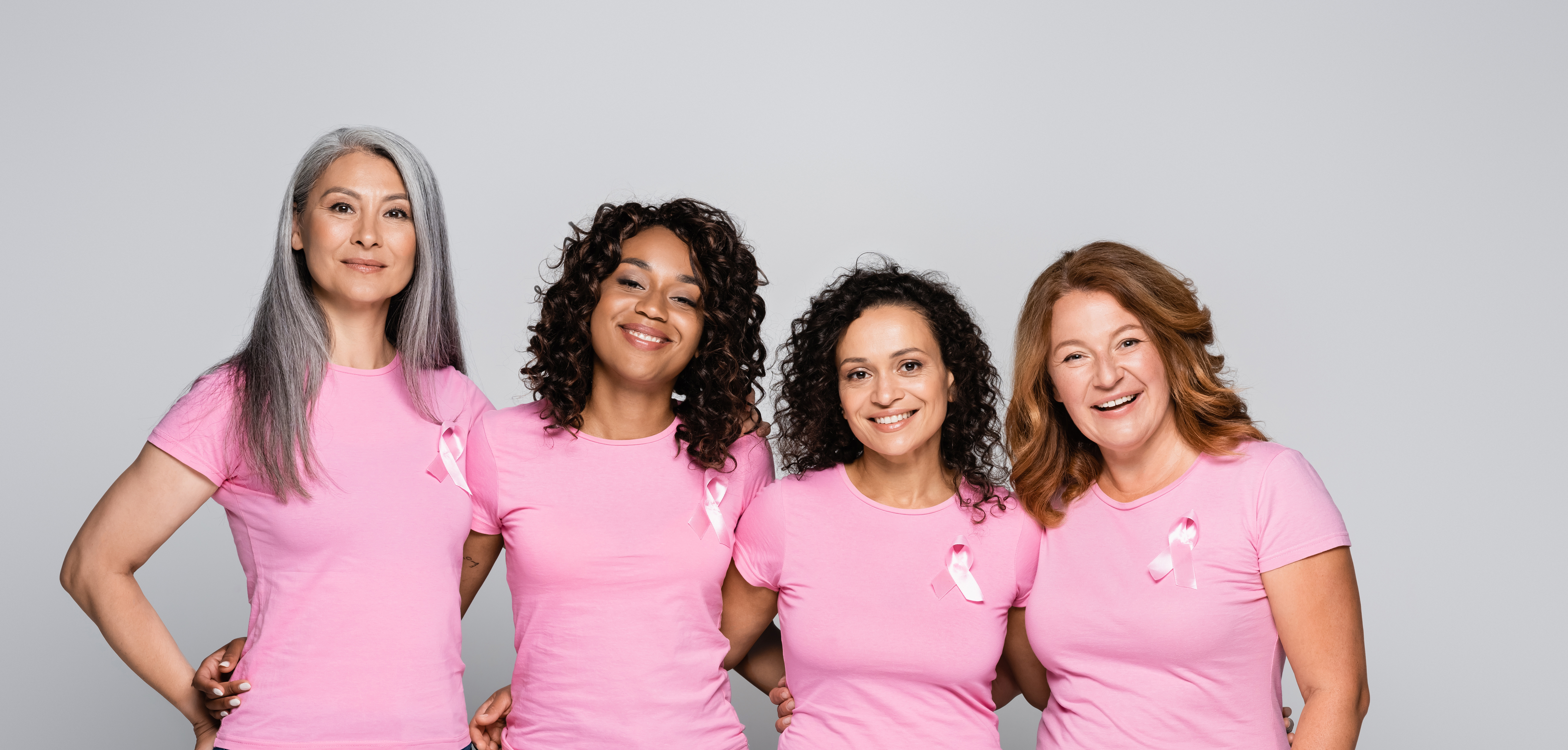 Four women wearing pink shirts with breast cancer awareness ribbons